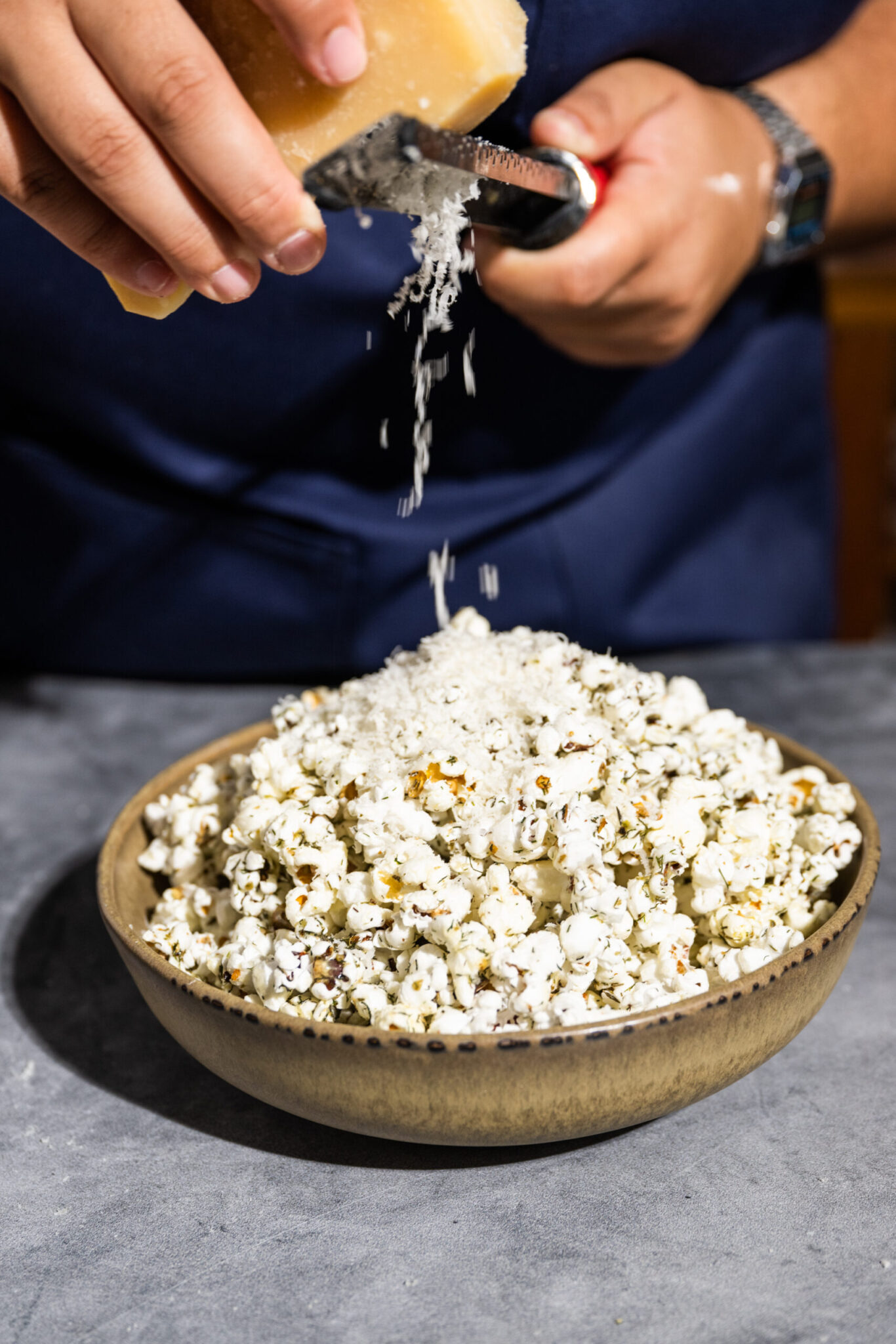 Grating Parmesan cheese on Herbed Weed Popcorn in a bowl