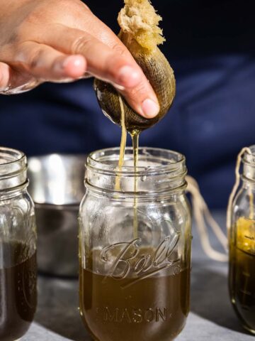 Squeezing infused oil from a cheesecloth sachet into a jar.